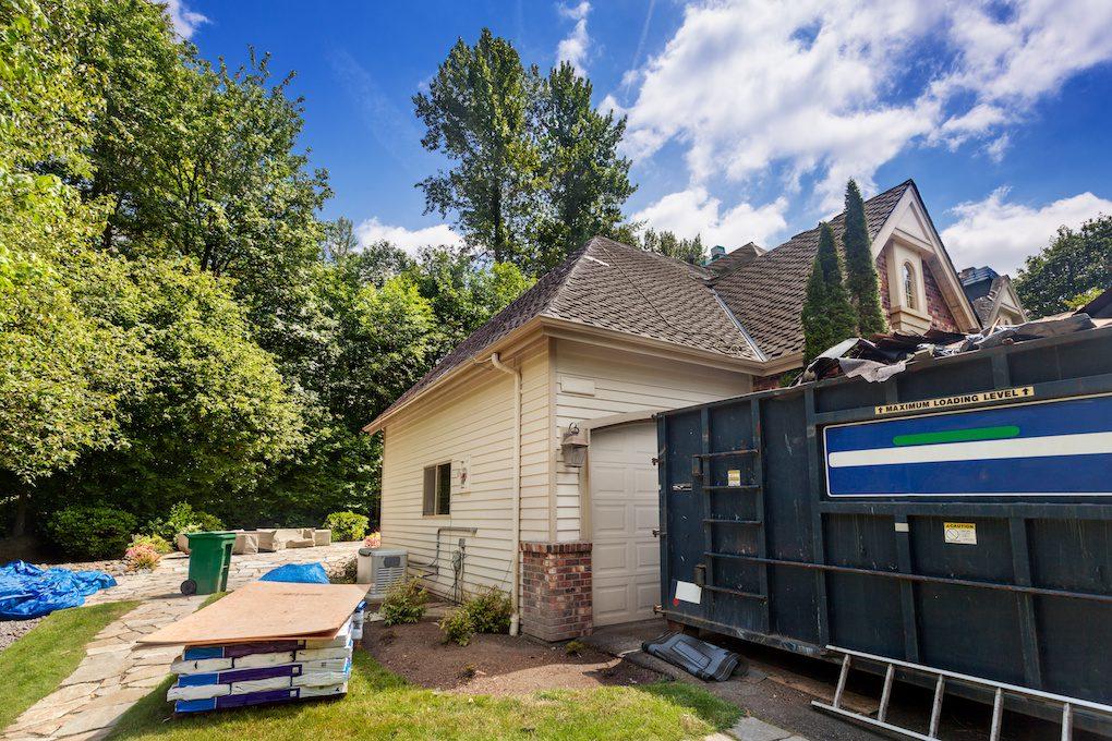 Suburban home in the middle of a roof tear off project, with dumpster there to collect debris
